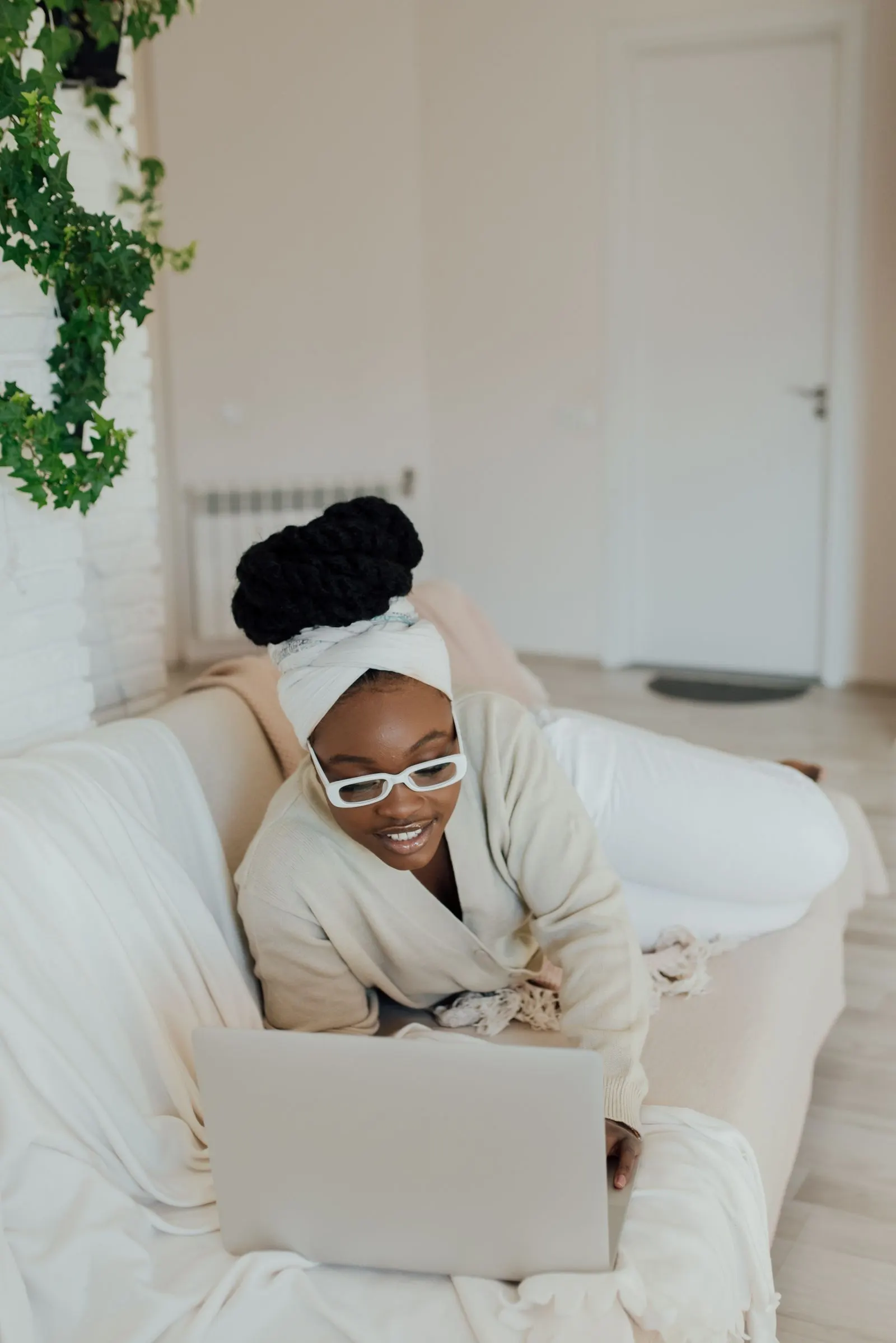 Smiling woman in glasses relaxing on a sofa while using a laptop at home