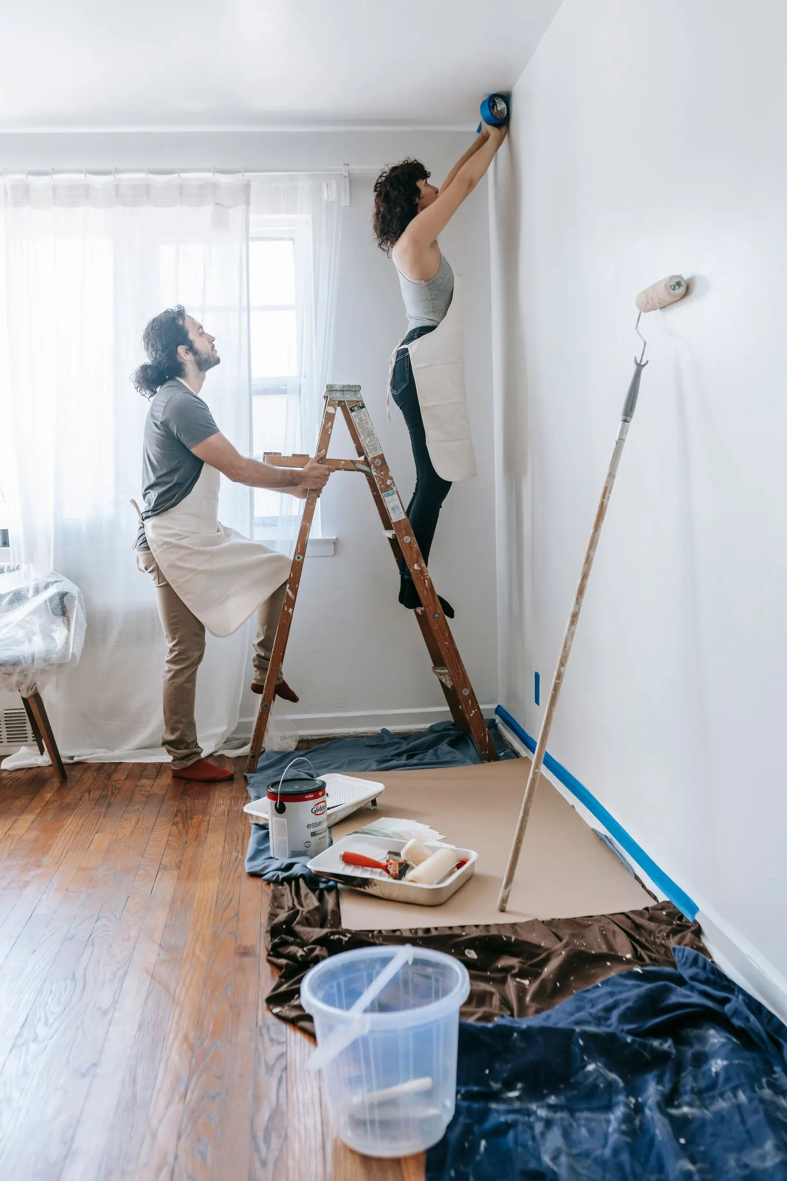 Two people painting the walls of a bright room during a home renovation