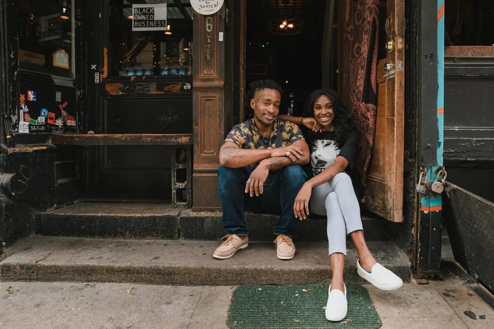 Smiling couple sitting on the front step of their small café
