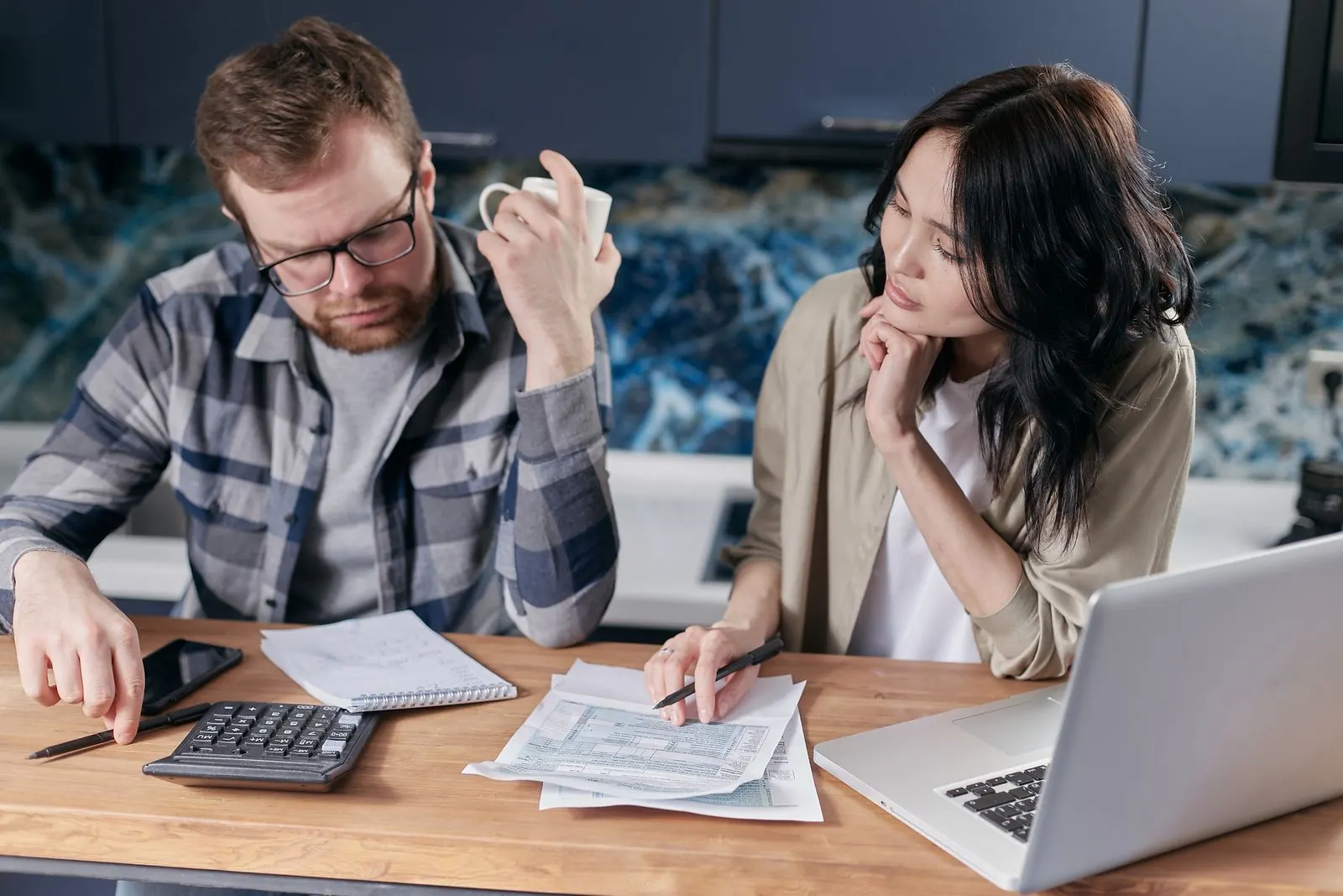 Couple at a kitchen table going over bills and paperwork with a laptop and calculator